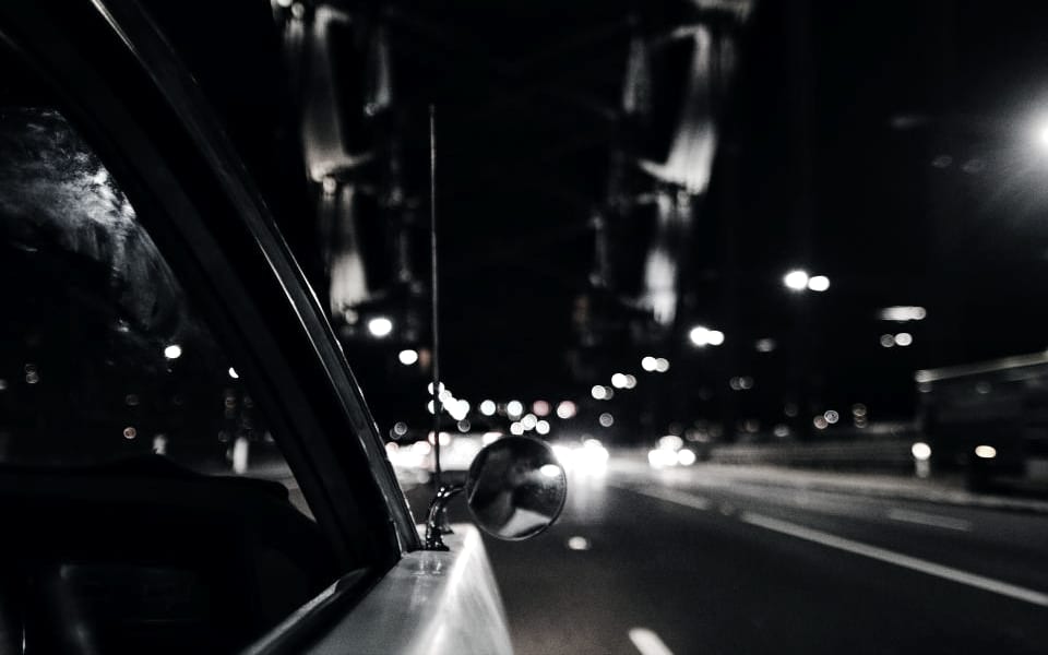 A city street at night, lit shopfronts along the road