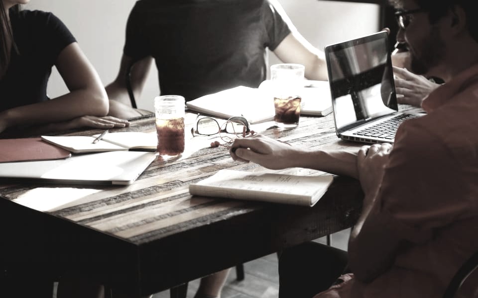 Three people working together around a table with laptops